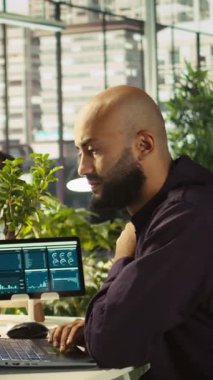 Görevdeki dikey video çalışanı laptopa bakarken başarıyı kutluyor ve başarılı sonuçlardan duyduğu heyecanı dile getiriyor. Adam olumlu iş başarısından mutlu, kamera B