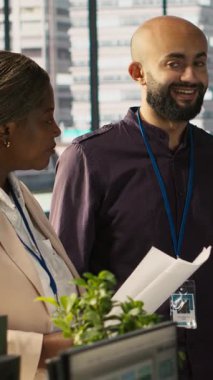 Dikey video Gevşetilmiş çok ırklı iş arkadaşları ofiste dokümanları incelerken, ölçümleri incelerken sohbet ederken eğleniyorlar. Gülümseyen çok ırklı meslektaşlar konuşuyor, birlikte çalışıyor, araştırıyorlar.