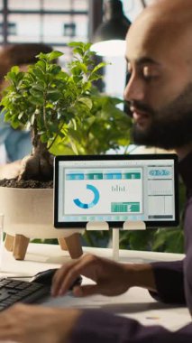 Ofis masasındaki masaüstü bilgisayarındaki belgeleri düzenleyen dikey video çalışanı, raporlar ve dosyalar güncelleniyor. İşçi masadaki bilgisayar ekranında veri grafiklerini analiz ediyor, istatistiksel bilgileri yorumluyor