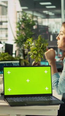 Ofis masasının üzerinde bilgisayardaki belgeleri düzenleyen çalışanların yanında dikey video yeşil ekran laptop var. Veri tablolarını analiz eden, istatistiksel bilgileri yorumlayan, B kamerasının yanındaki defter.