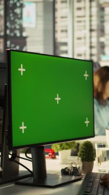 Ofisteki dikey videocu yeşil ekrandaki finansal grafikleri inceleyerek anahtar performans göstergelerini analiz ediyor. Çalışan, krom anahtar bilgisayarda veri eğilimlerine ve stratejik görüşlere göz atıyor