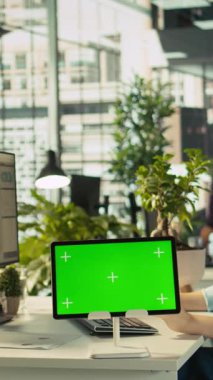 Çalışma masasında çalışan işçilerin iş vardiyası sırasında yeşil ekran tableti kullanarak görev çözdüğü dikey bir video. Ofis görevlisi iş yerinde krom anahtar aygıtı kullanarak e-posta iletişimi yapıyor