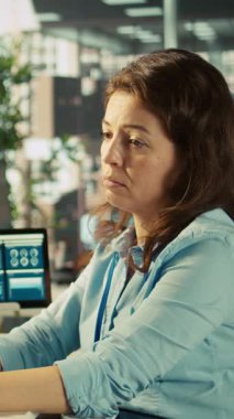 Ofisteki stresli çalışanın dikey videosu incelenemeyecek kadar çok belgenin yükü altında. İş yerindeki yorgun çalışanlar iş performans ölçümleri ve kamera B 'yi incelerken çok çalışılmış hissediyorlar.