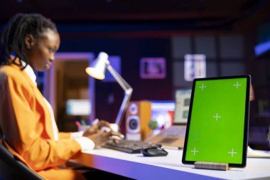 Not defteriyle evden çalışan bir kadın, not yazmak için yeşil ekran cihazı kullanıyor. Kişisel apartman ofisindeki uzaktan çalışan dizüstü bilgisayar kullanarak, model tabletindeki önemli bilgileri kopyalıyor