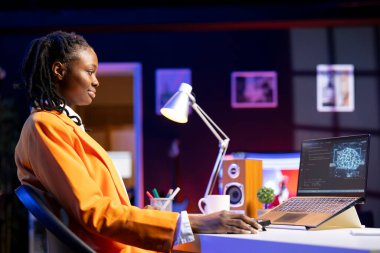 Dairede dizüstü bilgisayar kullanan gülümseyen kadın yapay zeka makinesini güncelliyor algoritmaları öğreniyor, kod yazıyor. Evden çalışan iyimser tele-çalışma bilişim uzmanı yapay zekayı yükseltmek için programlama kullanıyor