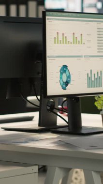 Dikey video Modern ofis çalışma masası bilgisayar monitörleri ile grafikler, grafikler ve veri analizleri, bitkiler ve şehir çevresi ile ilgili evrak ile çevrili, el kamerası