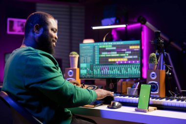 Besteci müzisyen şarkılarını bilgisayar yazılımında izole edilmiş bir akıllı telefon ekranıyla karıştırarak yeni bir müzik başlatıyor. Sanatçı konsolu karıştırma, oluşturma ve düzenleme üzerinde çalışıyor.