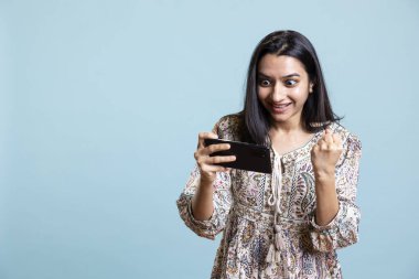 Kendine güvenen mutlu oyuncu gülümsüyor ve video oyunu yarışmasına dikkat ediyor. Cep telefonunda spor turnuvası var. Genç Hintli kadın stüdyoda interaktif oyun oynamaktan hoşlanıyor.