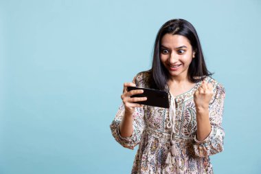 Kendine güvenen mutlu oyuncu gülümsüyor ve video oyunu yarışmasına dikkat ediyor. Cep telefonunda spor turnuvası var. Genç Hintli kadın stüdyoda interaktif oyun oynamaktan hoşlanıyor.