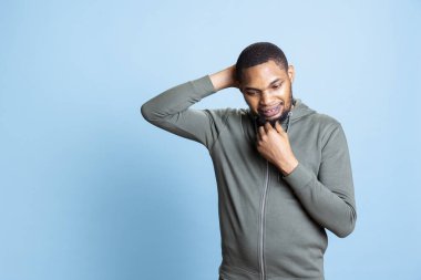 Gri kapüşonlu budala bir yetişkin. Çözümler ve yenilik için yeni fikirler düşünüyor. Mavi arka plana karşı düşünceleri var. Afrikalı Amerikalı adam stüdyoda tefekkür ediyor..