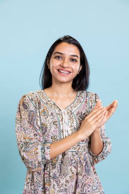 Hintli tatmin olmuş bir kadın el çırpıyor ve stüdyoda bir dönüm noktası olmaktan gurur duyuyor, başarısından memnun ve memnun. Gülümseyen yetişkin alkışları, zafer için tebrik ediyor..