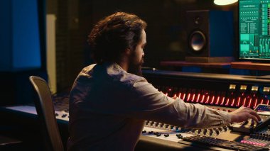 Müzik yapımcısının portresi kontrol odasında profesyonel stüdyoda çalışıyor ve ses kayıtlarını düzenliyor, konsol ile daw yazılımını ses geçirmez alanda karıştırıyor. Prodüksiyon sonrası ses mühendisi. Kamera A.