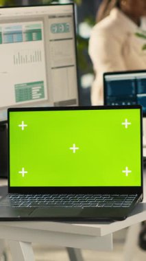 Ofis masasının üzerinde bilgisayardaki belgeleri düzenleyen çalışanların yanında dikey video yeşil ekran laptop var. Veri tablolarını analiz eden, istatistiksel bilgileri yorumlayan, kamera A 'nın yanındaki defter.