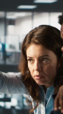 Dikey video çalışanı ve iş arkadaşı ofisteki bilgisayar gelirlerine bakıyor. Takım çalışma arkadaşları şirket istatistiksel numaralarını karşılaştırmaya odaklandı, son teslim tarihinden önce işi bitirmek için çok çalışıyorlar