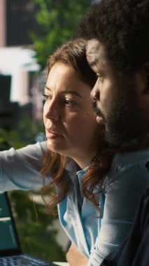 İşletme belgelerinde düzeltme yapmak için çalışan hatalarını gösteren dikey video ekip lideri. Afrika kökenli Amerikalı adam ve yönetici bilgisayar, kamera A kullanarak şirket bilgi kayıtlarını analiz ediyor.