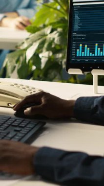 Ofisteki işçinin müşteriyle konuşmak için sabit telefonu kullanmasını gösteren dikey video. İş yerinde çalışan Afrikalı Amerikalı bir çalışan çağrı sırasında iş ortağıyla tartışıyor, performans ölçümlerini analiz ediyor.