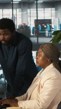 Dikey video ekibi çalışma arkadaşları masadaki bilgisayar ekranındaki veri tablolarını analiz ediyorlar. Masaüstü bilgisayarındaki hesap tablolarını tamamlayan çalışanlardan oluşan bir ekip verileri giriyor ve analiz ediyor, kamera A