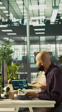 Finansal grafikleri inceleyen, kilit performans göstergelerini analiz eden dikey video Arap. Çalışma alanındaki Orta Doğulu çalışanlar veri eğilimlerine ve stratejik görüşlere bakıyor, kamera B