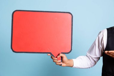 Otel kapıcısı kameranın önünde karton bir konuşma balonu tutuyor ve konukseverlik endüstrisi pazarlaması için boş ticari reklamlara işaret ediyor. Smokinli bir otelci. Kapat..