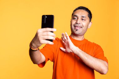 Rahatlamış bir adam, akıllı telefondan bir arkadaşıyla görüntülü konuşma yapıyor. Kaygısız Hintli adam telekonferansta arkadaşlarıyla konuşuyor..