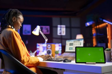 Merkez ofisteki telgraf çalışanı dizüstü bilgisayardaki istatistikleri kontrol ediyor, yeşil ekran tabletindeki verilerle karşılaştırıyor. Şirket gelir numaralarını analiz etmek için dizüstü bilgisayar ve model kroma anahtar aygıtı kullanan kişi