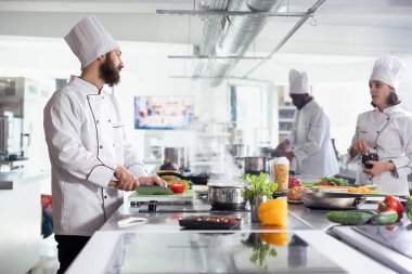 Yeşillik ve taze sebzeleri bıçakla kesen çeşitli aşçılar, restoran mutfağında yeni bir gurme yemeği için malzemeler hazırlıyorlar. İyi bir yemek deneyimi için profesyonel mutfak teknikleri..