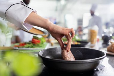 Kadın fırında gurme yemeği için baltayla biftek pişiriyor. Çiğ eti tavada maşayla çeviriyor. Mutfak uzmanı yağlı fileto ve gastronomi hazırlıyor. Kapat..