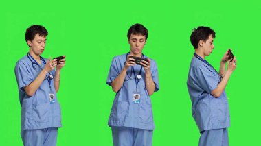 Akıllı telefon uygulamasında mobil video oyunu oynayan tıbbi asistan, sağlık hizmetlerine ara veriyor. Hemşire telefonda, yeşil ekran arkaplanının önünde duran bir oyun turnuvasından hoşlanıyor. Kamera B.