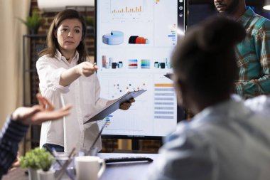 Odaklanmış iş kadını, modern teknoloji kullanılarak şirket araştırmalarında çeşitli grupları devreye sokan başlangıç stratejileri sunuyor. İş arkadaşları beyin fırtınası yapıyor ve girişimciyi dinliyor..