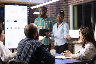 Çok ırklı iş arkadaşları, mali raporda kaydedilen ilerlemeyi izlemek ve proje planlarını tamamlamak için etkin bir şekilde çalışıyorlar. Afrika kökenli Amerikalı çalışanlar gece yarısı grup toplantısında iş sunumu yapıyorlar..