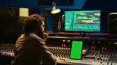 Müzik yapımcısı ses yazılımında ses kaydediyor, karıştırıyor ve kopyalıyor, ses düzeyini arttırmak ve melodileri yükseltmek için stereo konsol ve anahtarlar kullanıyor. Tablette yeşil ekran görüntüsü. Kamera B.