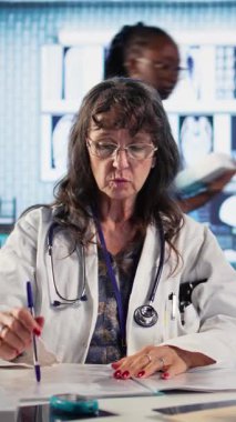 Dikey video başhekimi ve hasta modern bir tıp ofisinde teşhis sonuçlarını tartışıyor, gelişmiş teknolojiyi x ışınları ve MRI taramalarını gösteren kayıtlar kullanarak sergiliyorlar. Bakım yönetimi