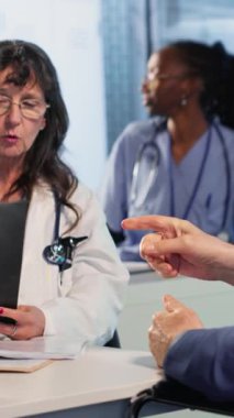 Dikey Video Kadını doktoru konsültasyon sırasında tekerlekli sandalye kullanıcısına hastalık ve tedavi planını sunuyor. Hekim sigorta altında tarama yorumu yapıyor. Eksiklik