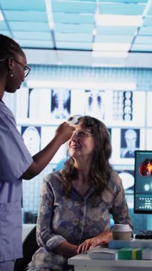 Dikey Afrikalı Amerikalı hemşire check-up 'taki hastaya ateş ölçer ve kabinedeki doktora yardım teklif eder. Tıp personeli teşhis araçları ve araçlar kullanıyor, hastalık önleme