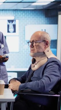 Dikey video personeli yaşlı tekerlekli sandalye kullanıcısına boyun tasması takarak, termometreyle ateş ölçümleri yaparak danışmanlık yapıyor. Maluliyet dostu kabinede uzman danışmanlığı. Kamera A.