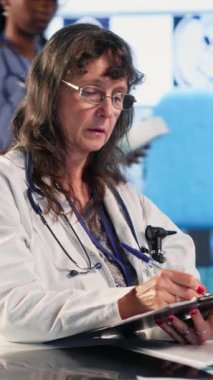 Dikey Görüntü Uzmanı, yaşlı bir hastanın sağlık kontrolündeki test sonuçlarıyla tanıları açıklıyor, kıdemli bir adamla tarama yapıyor. Tesisteki sağlık hizmetleri