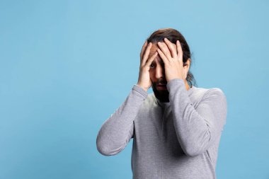 Dehşete düşmüş genç bir adam bir şeylerden korkuyor ve endişeleniyor. Mavi arka planda perişan ve korkmuş. Korkudan ödü kopan adam, korku reaksiyonu.