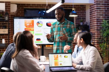 Afrika kökenli Amerikalı yönetici, gece geç saatlerde tuğla duvar çalışma alanında iş arkadaşlarıyla tartışıyor. Başlangıçta pazarlama stratejisini incelemek için dijital aygıtlar kullanan çok ırklı meslektaşlar.