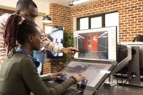 Ofis masasında yenilikçi fikirleri tartışan Afrikalı Amerikalı iş arkadaşları web sitesi geliştirmek için grafik yazılım kullanıyorlar. Siyah erkek yönetici ekranı işaret ederek, kadın çalışana dijital araçları açıklıyor.