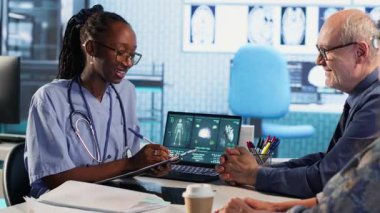 Kadın hemşire ve hastalar, tıbbi muayenehanede teşhis sonuçlarını inceliyor, gelişmiş sağlık teknolojisi kullanarak x ışını görüntüleme sonuçlarını ve MRI taramalarını değerlendiriyor. Sigortayı kontrol et. Kamera B.