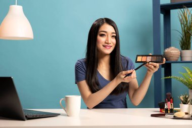 Asyalı güzellik vlogcusu canlı yayında kozmetik ürünlerini sunuyor, abonelerine eleştiriler veriyor. Genç bir kadın video blogunda en son göz farı rengini tartışıyor..