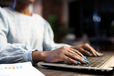 Afrika kökenli Amerikalı iş kadını bir ofis masasındaki bilgisayarına önemli veriler giriyor. İşindeki hassasiyeti vurgulamak için parmaklarını klavyeye koyuyor..