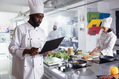 Kendini adamış Afrikalı Amerikalı şef laptopta gurme yemekleri pişirmek, restoranın mutfağında lezzetli yemekler yapmak için araştırma yapıyor. Genç adam yemek hazırlıyor..