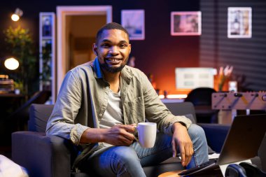 Sabah işe gitmeden önce taze kahveyi yudumlayan, rahat dairesinden uzaktan kumandalı işten zevk alan siyah adam. Genç yetişkin kendini mutlu ve mutlu hissediyor, birden fazla iş yapıyor..