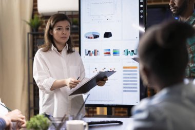 İş planlama için finansal tablolar ve dijital cihazlar kullanarak, beyaz kadın yöneticiler, oturduğu meslektaşlarına proje stratejileri sunuyor. Profesyonel kadın araştırma fikirlerini paylaşıyor.