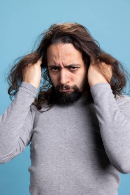 Ortadoğulu adam çaresiz davranıyor ve kamera önünde saçını çekiyor. Mavi arka plana karşı öfkeli ve stresli. Genç yetişkin duyguları bunalmış ve çaresizlik içinde..