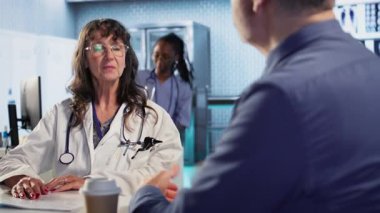 Yaşlı bir erkek hastayla yapılan doktor toplantısında kabinede sonuçları tartışmak için röntgen taramaları ve sonuçları yorumlamak için gelişmiş teşhis araçları kullanılıyor. Profesyonel sağlık yaklaşımı. Kamera A.