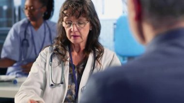 Kıdemli kadın, doktoruyla birlikte teşhis sonuçlarını kabinede değerlendiriyor. Hastasına doğru sonuçları vermek için ileri teknoloji aletleri kullanıyor. Tıp endüstrisinde bakım yönetimi. Kamera B.