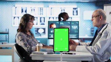 Kabinedeki hasta kadına tıbbi danışmanlık yapıyor. İzole edilmiş maket ekranı var. Başka bir röntgen taraması için hastane kayıtlarını kontrol ediyor. Yaşlı hasta doktoruyla konuşuyor. Kamera A.