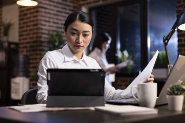Şirket ofisinde çalışan kendini işine adamış bir kadın. Tabletteki iş raporlarını inceliyor. Masasında dijital cihazlarla çevrili Asyalı yönetici, gece proje planlamasına odaklandı.